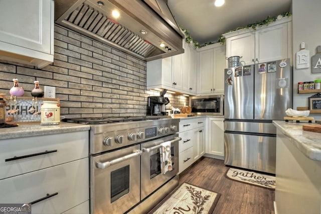 kitchen with tasteful backsplash, white cabinetry, stainless steel appliances, dark wood-type flooring, and wall chimney exhaust hood