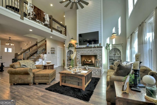 living room featuring a high ceiling, a brick fireplace, hardwood / wood-style floors, and ceiling fan