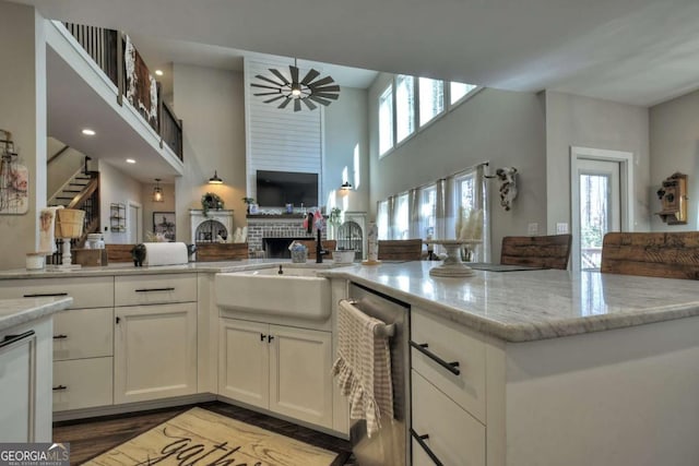 kitchen with sink, a brick fireplace, ceiling fan, light stone countertops, and white cabinets