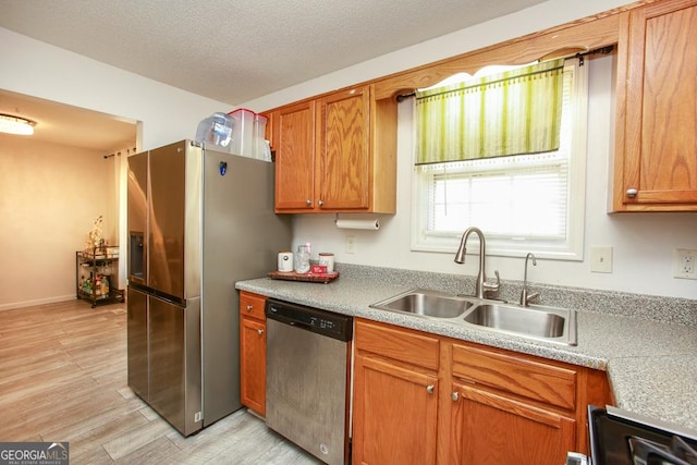 kitchen featuring stainless steel appliances, sink, a textured ceiling, and light wood-type flooring