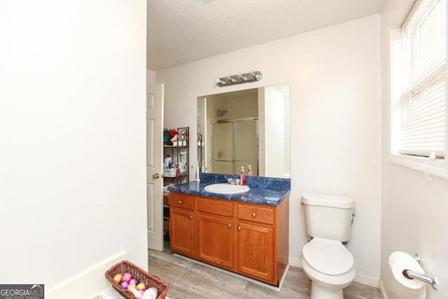 bathroom with a shower with door, vanity, a textured ceiling, and toilet