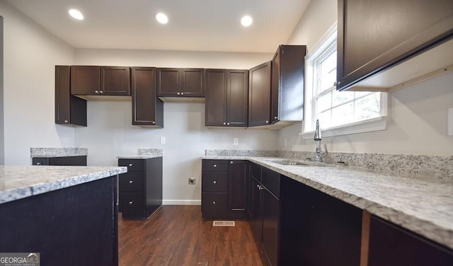 kitchen with sink, dark wood-type flooring, dark brown cabinets, and light stone countertops