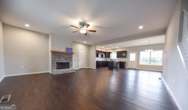 unfurnished living room with ceiling fan with notable chandelier, a fireplace, and dark hardwood / wood-style floors