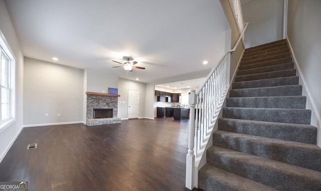 stairs with a stone fireplace, dark hardwood / wood-style floors, and ceiling fan