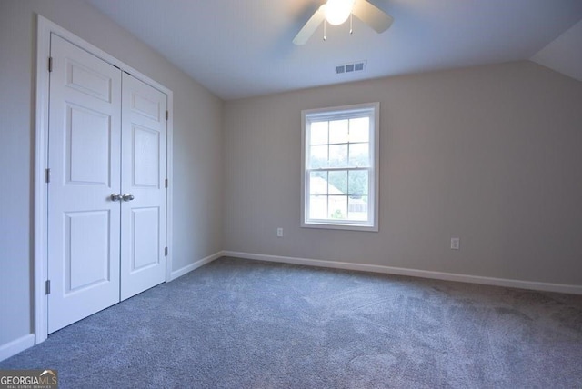 unfurnished bedroom with ceiling fan, lofted ceiling, a closet, and dark colored carpet