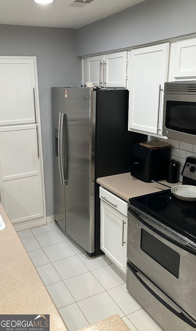 kitchen featuring stainless steel appliances, white cabinetry, light tile patterned floors, and backsplash