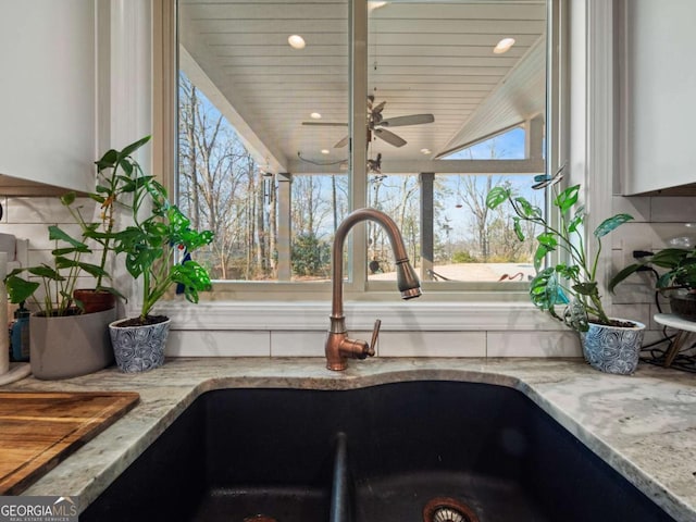 room details featuring ceiling fan, light stone countertops, sink, and white cabinets