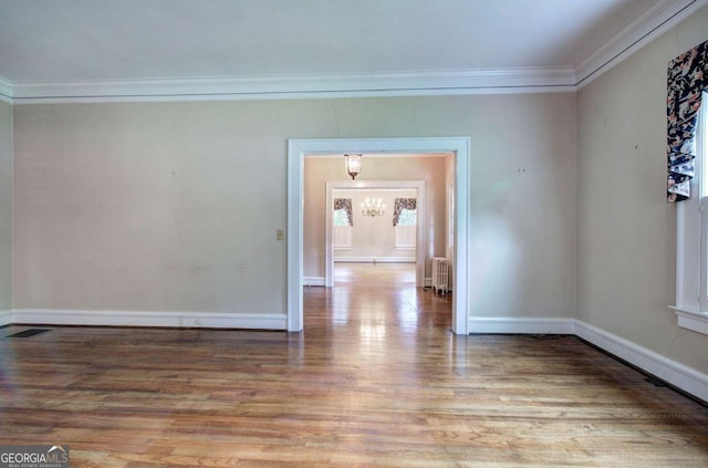 empty room with ornamental molding, radiator heating unit, an inviting chandelier, and light hardwood / wood-style flooring