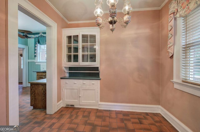 unfurnished dining area featuring an inviting chandelier, crown molding, and dark tile patterned floors