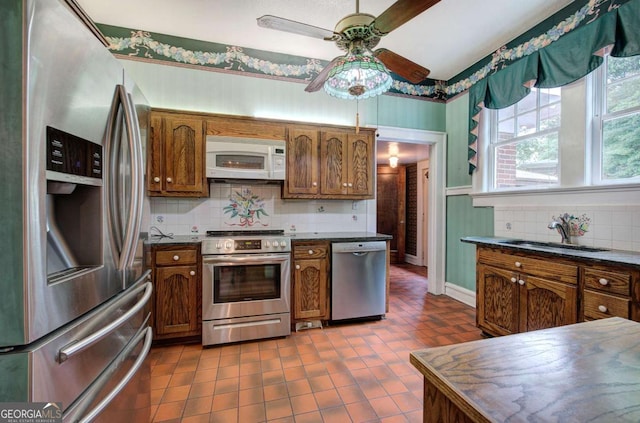 kitchen with sink, dark tile patterned floors, ceiling fan, backsplash, and stainless steel appliances