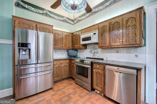 kitchen with appliances with stainless steel finishes, backsplash, dark stone counters, ceiling fan, and tile patterned floors