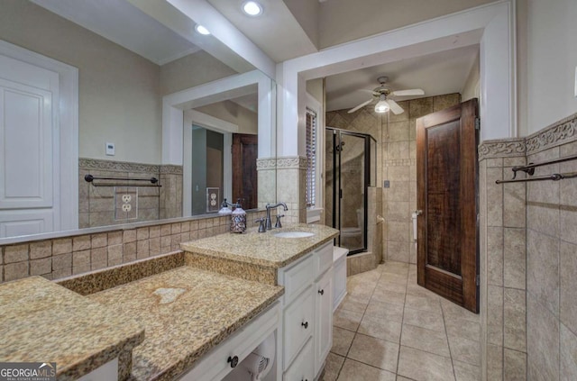 bathroom with a shower with shower door, tile walls, tile patterned flooring, vanity, and ceiling fan