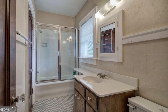 full bathroom featuring vanity, tile walls, bath / shower combo with glass door, and toilet