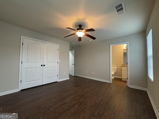 unfurnished bedroom featuring ensuite bathroom, dark hardwood / wood-style floors, ceiling fan, and a closet