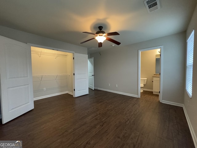 unfurnished bedroom featuring ceiling fan, ensuite bathroom, dark hardwood / wood-style flooring, and a closet