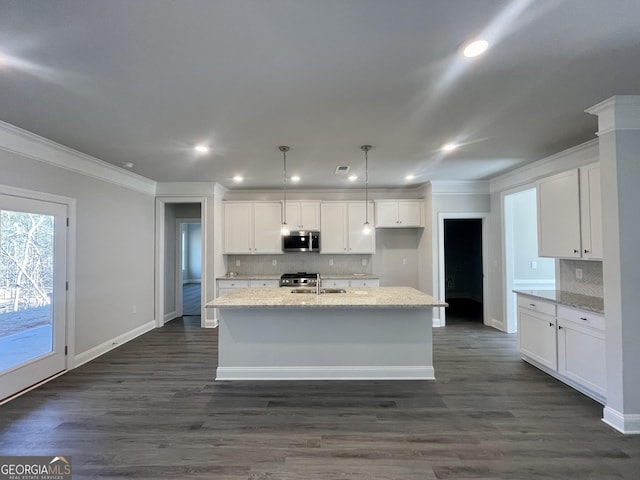 kitchen with light stone counters, decorative light fixtures, stainless steel microwave, white cabinets, and an island with sink