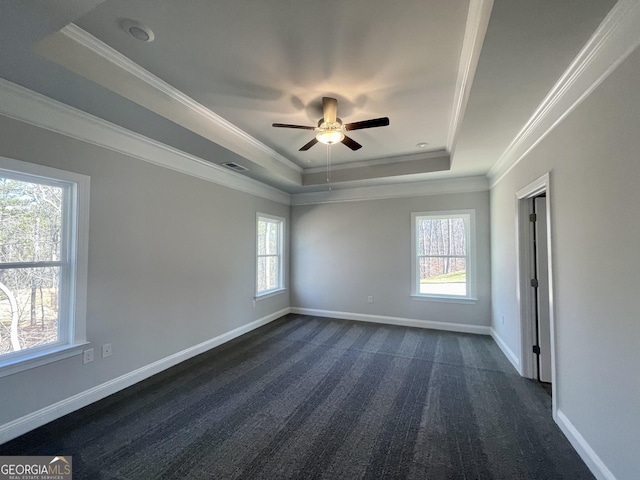 empty room with baseboards, a tray ceiling, dark carpet, and crown molding