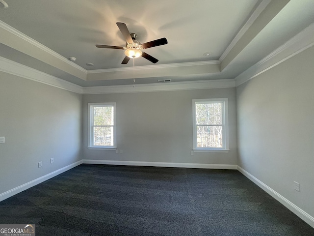 spare room with baseboards, a tray ceiling, dark colored carpet, and crown molding