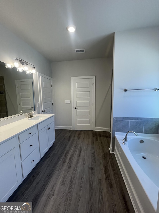 bathroom featuring a bath, baseboards, wood finished floors, and vanity