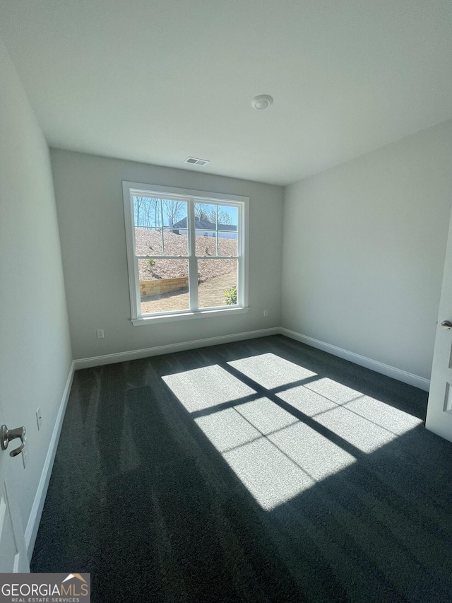 unfurnished room with visible vents, dark carpet, and baseboards