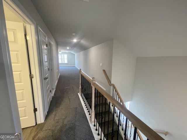 corridor with dark colored carpet, vaulted ceiling, and an upstairs landing