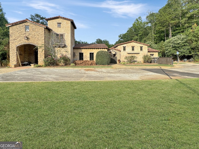 mediterranean / spanish-style house with stone siding, a tile roof, a front lawn, and stucco siding