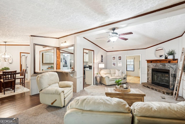 living room with ceiling fan with notable chandelier, a fireplace, lofted ceiling, crown molding, and a textured ceiling