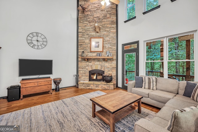 living room featuring a towering ceiling, a stone fireplace, and hardwood / wood-style floors