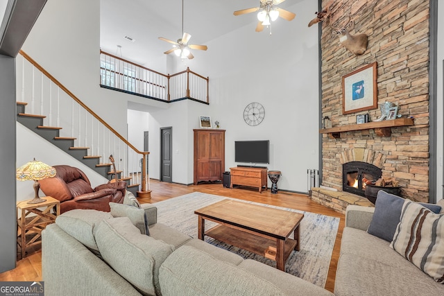 living room with ceiling fan, a fireplace, light hardwood / wood-style flooring, and a towering ceiling