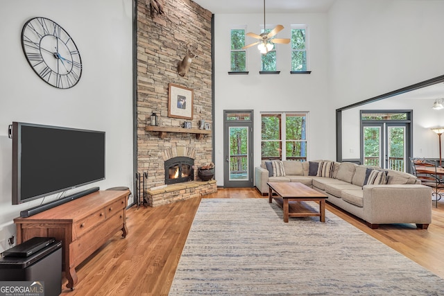 living room featuring a stone fireplace, ceiling fan, and light wood-type flooring