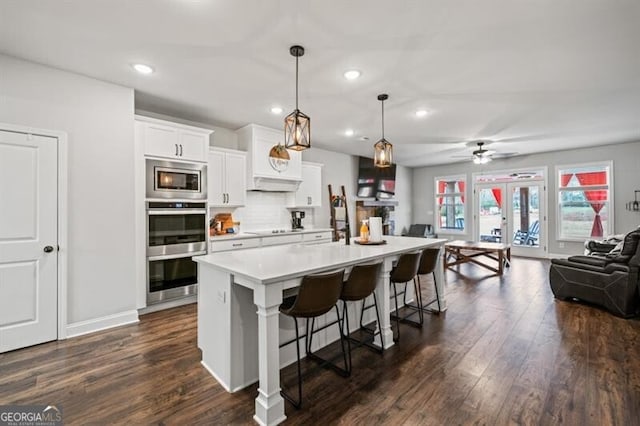 kitchen featuring a breakfast bar, white cabinetry, hanging light fixtures, appliances with stainless steel finishes, and an island with sink