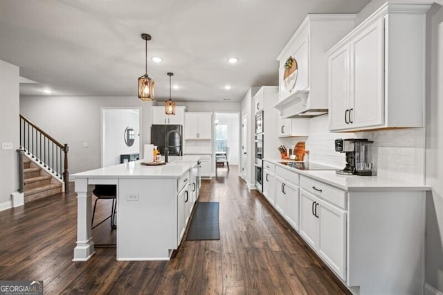 kitchen featuring a kitchen bar, white cabinetry, decorative light fixtures, an island with sink, and black appliances