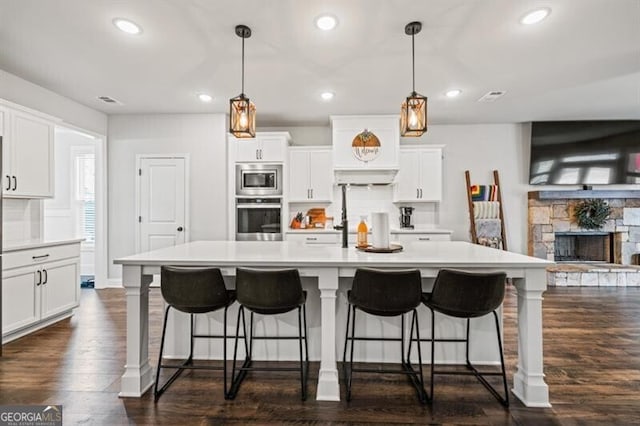 kitchen with stainless steel appliances, an island with sink, white cabinets, and decorative light fixtures