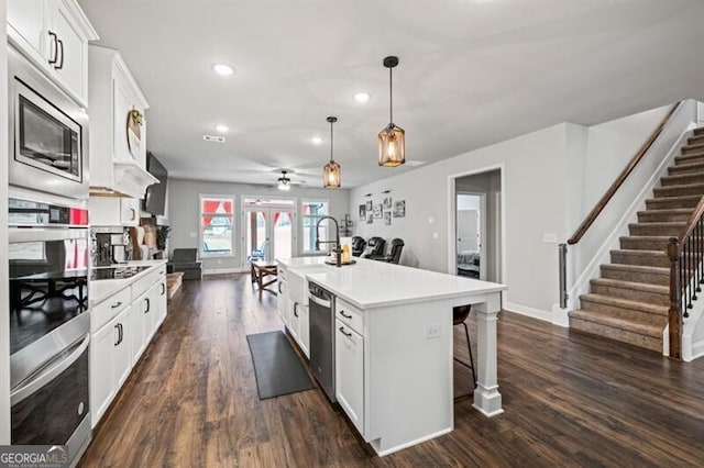 kitchen with a kitchen bar, pendant lighting, stainless steel appliances, a kitchen island with sink, and white cabinets