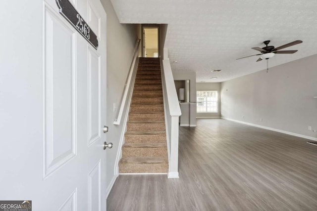 staircase with ceiling fan, wood-type flooring, and a textured ceiling