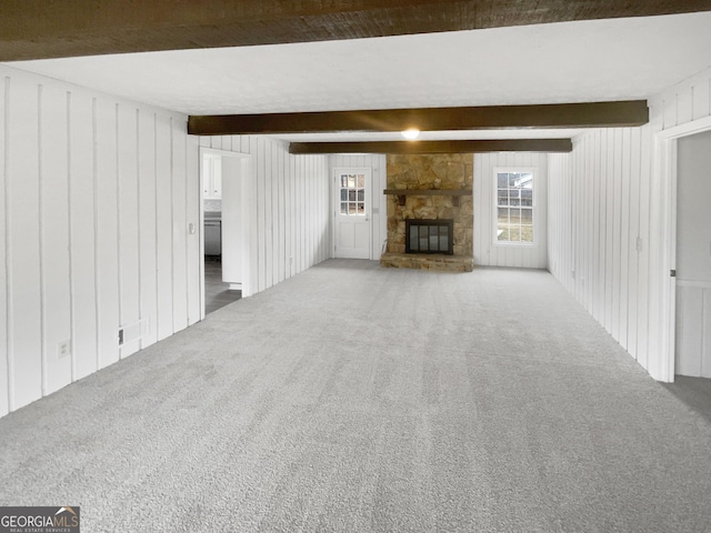 unfurnished living room featuring a stone fireplace, beamed ceiling, and carpet flooring