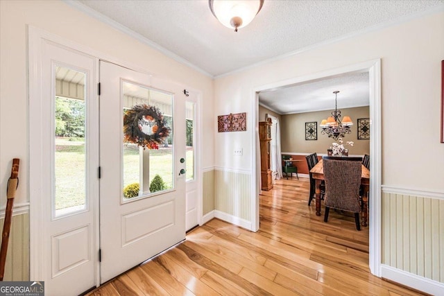 entryway with ornamental molding, a chandelier, hardwood / wood-style floors, and a textured ceiling