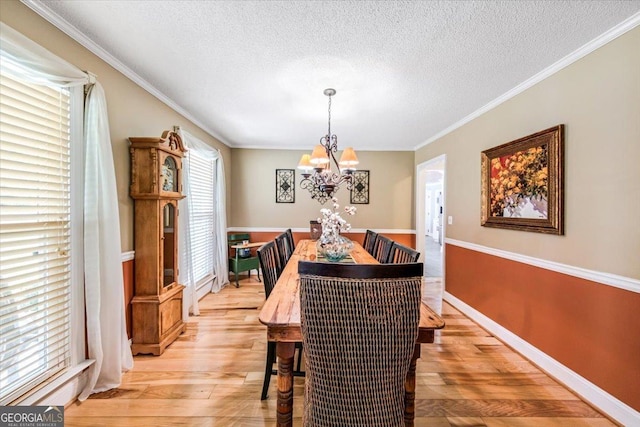 dining area featuring crown molding, a textured ceiling, a notable chandelier, and light hardwood / wood-style floors