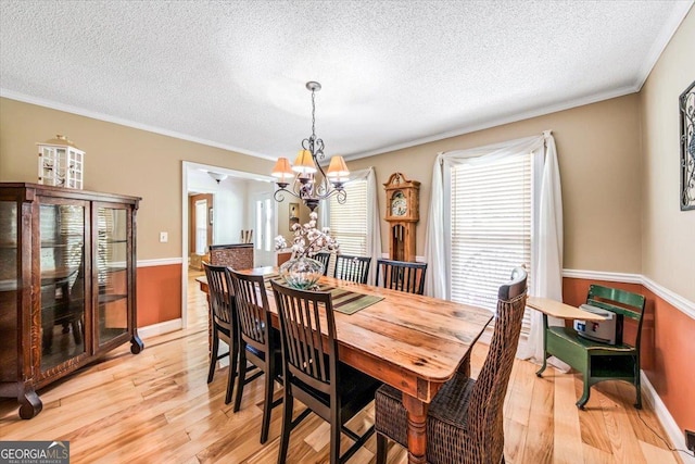 dining area featuring ornamental molding, a chandelier, a textured ceiling, and light wood-type flooring