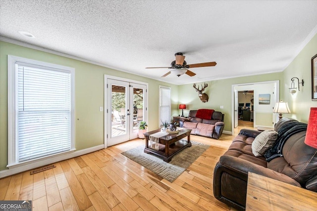 living room featuring french doors, ornamental molding, ceiling fan, a textured ceiling, and light hardwood / wood-style flooring