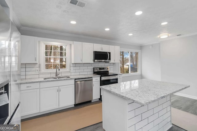 kitchen featuring sink, appliances with stainless steel finishes, white cabinetry, a center island, and light stone counters