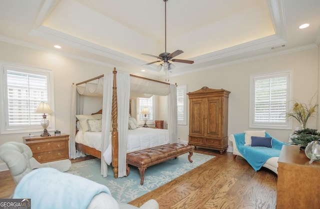 bedroom featuring a raised ceiling, hardwood / wood-style flooring, and multiple windows