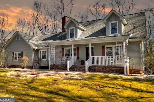 cape cod home featuring a porch, roof with shingles, a lawn, and a chimney