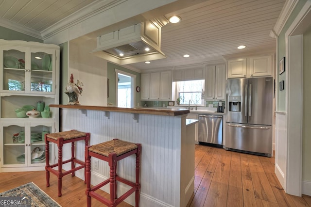 kitchen featuring appliances with stainless steel finishes, white cabinetry, a kitchen breakfast bar, kitchen peninsula, and crown molding