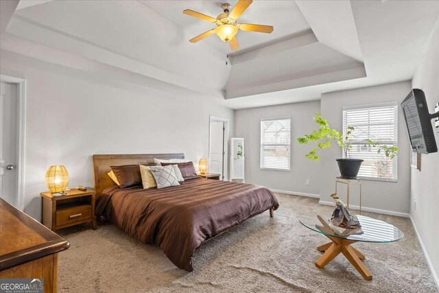 bedroom featuring a raised ceiling, light colored carpet, and ceiling fan