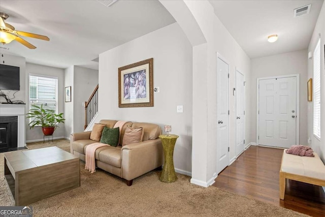 living room with arched walkways, a fireplace with flush hearth, visible vents, baseboards, and stairway