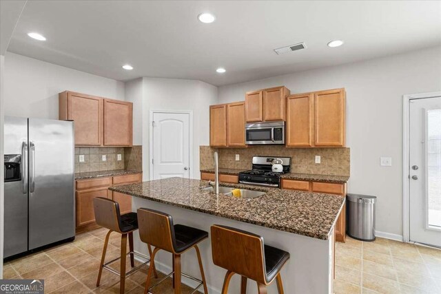 kitchen with appliances with stainless steel finishes, a kitchen bar, an island with sink, and dark stone countertops