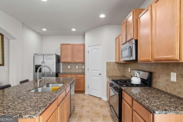 kitchen with sink, stainless steel appliances, dark stone counters, and a center island with sink