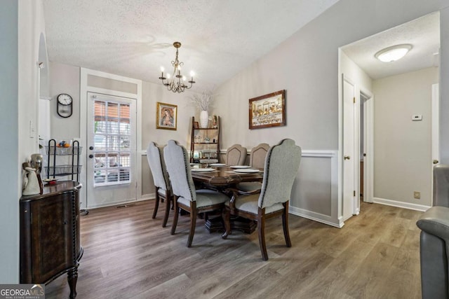 dining area with hardwood / wood-style flooring, an inviting chandelier, and a textured ceiling