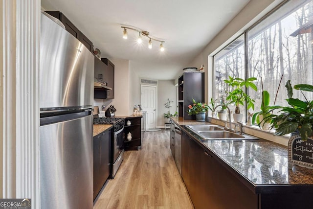 kitchen featuring appliances with stainless steel finishes, light hardwood / wood-style floors, sink, and dark stone countertops